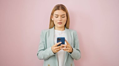 Genç sarışın iş kadını, izole edilmiş pembe arka plan üzerinden akıllı telefondan konuşuyor.
