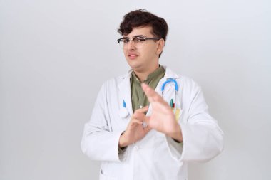 Doktor üniforması ve steteskop takan genç, tiksindirici ve tiksindirici bir yüz ifadesi takınan, tiksindirici bir yüz ifadesi takınan. Eller havada. 