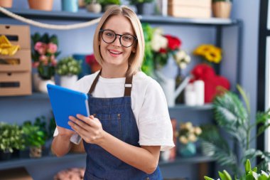 Young blonde woman florist smiling confident using touchpad at florist shop