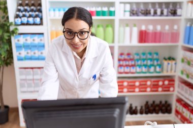 Genç Arap kadın eczacı. Eczanede bilgisayar kullandığından emin gülümsüyor.