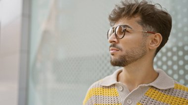 Havalı genç Arap adam, güneş gözlüklü, şehir sokağında ciddi bir ifadeyle yan yana, rahat yaşam tarzını yaşarken güneşli açık hava ortamının altında güneşleniyor.