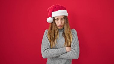 Kafkasyalı genç bir kadın üzgün duruyor, izole kırmızı arka planda noel şapkası takıyor.
