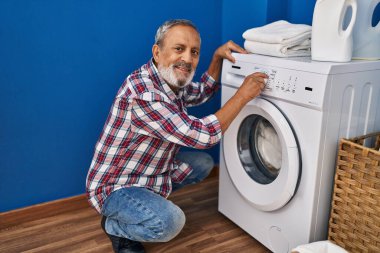 Yaşlı, gri saçlı, gülümseyen, kendine güvenen, çamaşır makinesini çalıştıran adam.