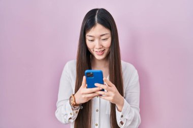 Çinli genç bir kadın, mutlu ve havalı bir gülümseme ile gülümseyen akıllı telefon yazma mesajı kullanıyor. diş gösterme. 