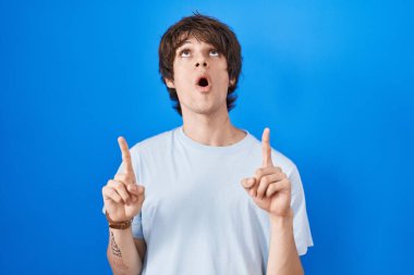 Mavi arka planda duran İspanyol genç adam şaşırmış ve şaşırmıştı. Yukarı baktı ve parmaklarıyla işaret etti ve kollarını kaldırdı.. 