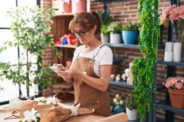 Çiçekçide akıllı telefon kullanan orta yaşlı bir kadın.