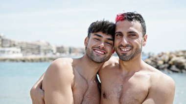 İki erkek turist gülümsüyor. Kumsalda birbirlerine sarılıyorlar.