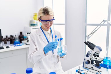 Genç sarışın bilim adamı laboratuarda test tüplerini inceliyor.