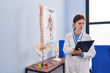 Genç sarışın kadın pisiyoterapist rehabilitasyon kliniğindeki panoya omurga yazısının anatomik modelini gösteriyor.