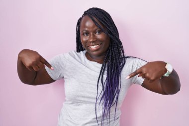 Pembe arka planda duran genç Afrikalı bir kadın. Kendine güveni tam görünüyor. Kendini gururlu ve mutlu bir şekilde gösteriyor.. 