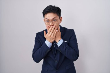 Genç Asyalı takım elbiseli ve kravatlı bir adam yanlışlıkla elleri ile ağzını kapatırken şok oldu. gizli kavram. 
