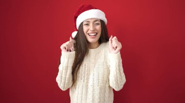 Genç, güzel İspanyol kadın, kendine güvenen, kendine güvenen, kırmızı arka planda bir Noel şapkası takan.