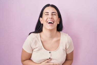 Pembe arka planda dikilen genç İspanyol kadın gülümsüyor ve kahkahalarla gülüyor.. 