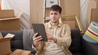 Yeni evindeki kanepede tablet kullanan İspanyol genç adam.