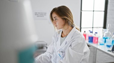 Ciddi bir yüz ifadesiyle odaklanmış genç sarışın kadın bilim adamı. Çığır açan laboratuvar araştırmalarına dalmış, sessiz bir klinikte tek başına oturuyor..