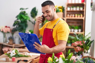 Genç İspanyol çiçekçi, çiçekçide akıllı telefondan pano okuyor.