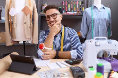 Atölyede çalışan, sakallı terzi İspanyol adam kameraya kollarını kavuşturmuş ve çenesini kaldırmış gülümsüyor. Olumlu düşünmek. 