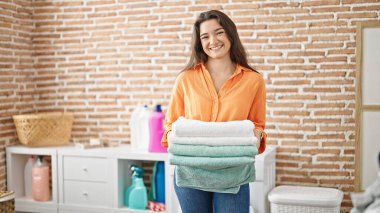 Çamaşırhanede gülümseyen katlanmış havluları tutan güzel İspanyol kadın.