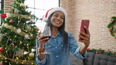 Afro-Amerikalı kadın akıllı telefonla selfie çekiyor evde Noel 'i kutlamak için şarap içiyor.