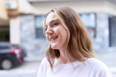 Beyaz kadın gülümsüyor. Kendinden emin. Caddenin kenarına bakıyor.