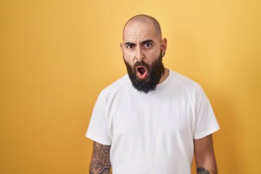 Sakallı ve dövmeli genç bir İspanyol şokta, sarı arka planda duruyor. Şüpheci ve alaycı görünüyor, ağzı açık kalmış. 