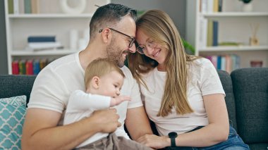 Anne, baba ve bebeğin ailesi evdeki kanepede otururken gülümsüyor.