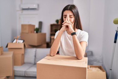 Young beautiful hispanic woman leaning on package with worried expression at new home
