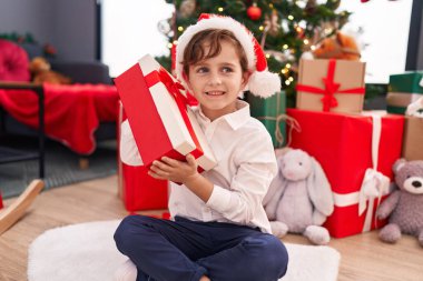 Sevimli İspanyol çocuk evde Noel ağacının yanında yerde oturan hediye sesini duyuyor.