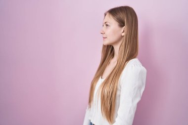 Young caucasian woman standing over pink background looking to side, relax profile pose with natural face and confident smile. 