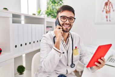 Genç İspanyol doktor dokunmatik ped kullanıyor. Klinikte Samrtphone ile konuşuyor.