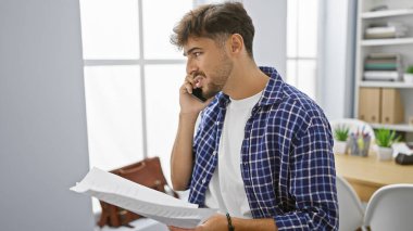 Odaklanmış genç bir Arap, bir iş adamı, ofiste akıllı telefonuyla ciddi bir konuşma yaparken bir belgeyi okumaya dalmış.