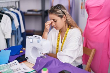 Young blonde woman tailor stressed using sewing machine at clothing shop