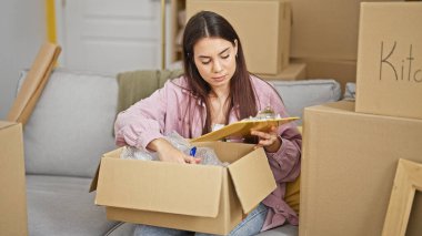 Genç, güzel, İspanyol bir kadın yeni evindeki panoda karton kutuları açıyor.