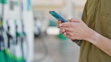 Genç İspanyol adam benzin istasyonunda akıllı telefon kullanıyor.