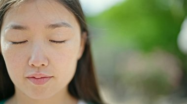 Young chinese woman breathing with closed eyes at park