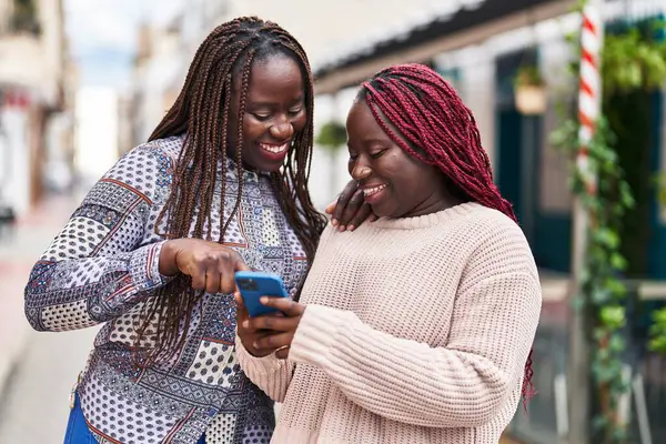 African american women friends smiling confident using smartphone at street