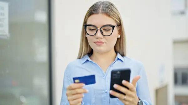 Young blonde woman business worker shopping with smartphone and credit card at street