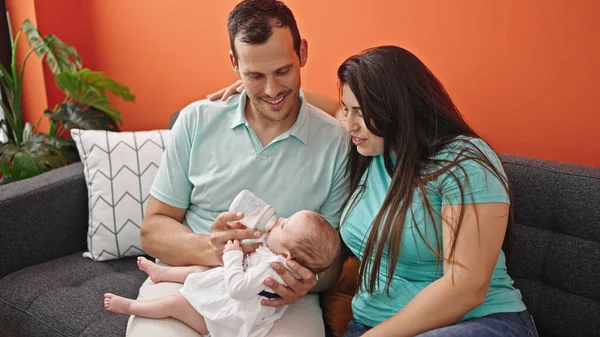 三个喂养婴儿的家庭坐在家里的沙发上 — 图库照片