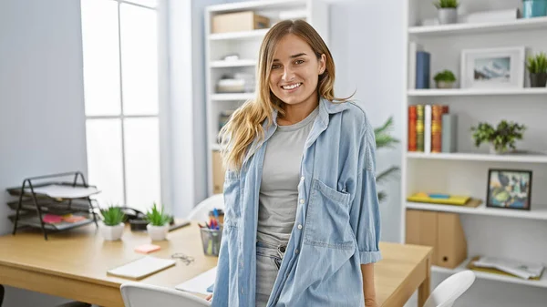 ブロンド 若くて自信のある女性は 彼女のエレガントなビジネス職場で笑顔を感じ 屋内オフィスで積極的に成功を放射します — ストック写真