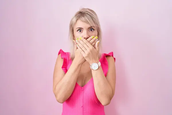 ピンクの背景の上に立つ若い白人女性は間違いのために手で口をカバーショックを受けた 秘密の概念 — ストック写真
