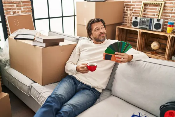 Middle age man drinking coffee holding test color paint at new home