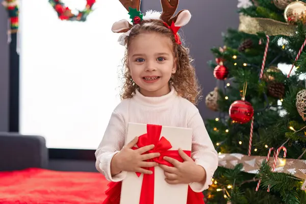 愛らしいブロンドの少女は自宅でクリスマスツリーで立っているギフトを抱擁 — ストック写真