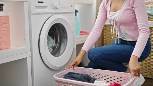 African american woman washing clothes holding basket with clothes at laundry room
