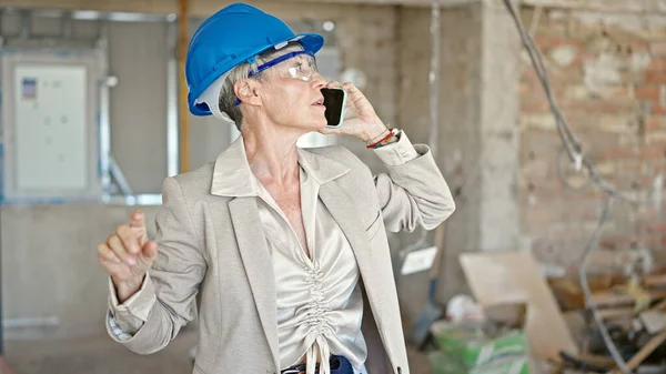 Middle age blonde woman architect talking on smartphone at construction site
