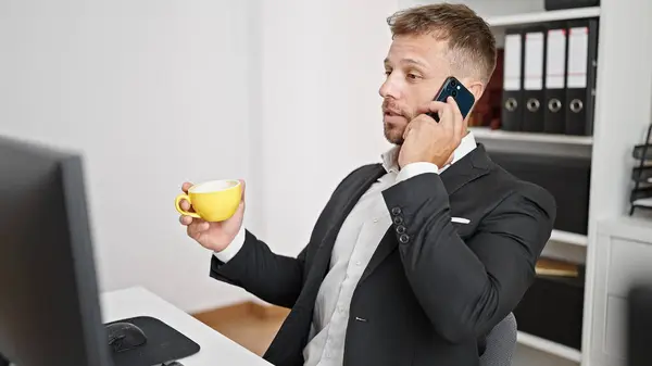 Young man business worker talking on smartphone drinking coffee at office