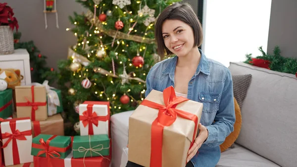 年轻的高加索女人抱着圣诞礼物坐在家里的沙发上 — 图库照片