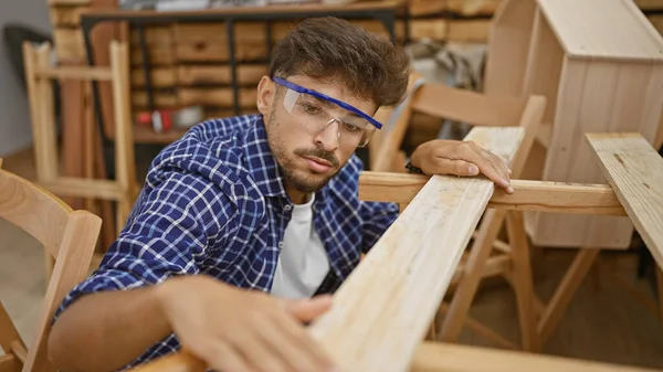 Hard-at-work, handsome young arab carpenter focused on woodworking job, touching plank in carpentry workshop