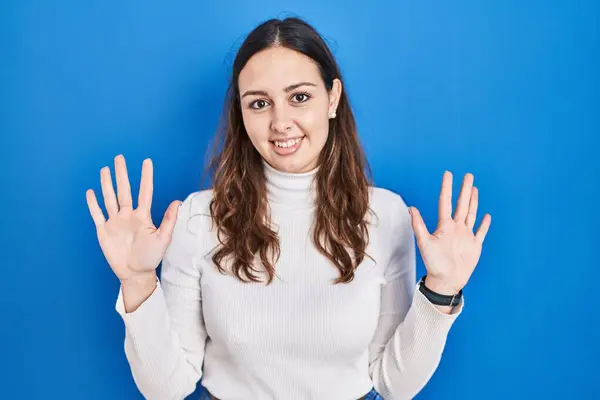 stock image Young hispanic woman standing over blue background showing and pointing up with fingers number ten while smiling confident and happy. 