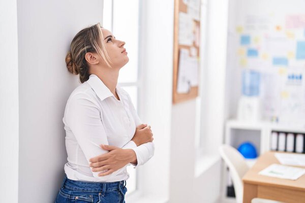 Молодая блондинка-бизнес-работница, стоящая со скрещенными руками в офисе