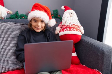 Evdeki yılbaşı dekorasyonunda dizüstü bilgisayar kullanan sevimli İspanyol çocuk.